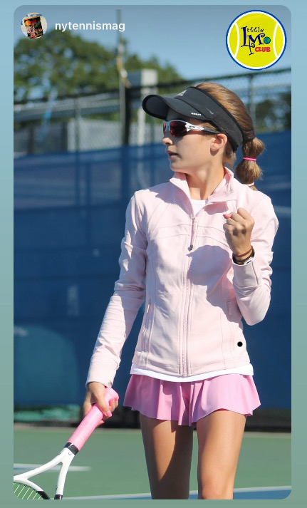 Female tennis player wearing pink skirt, jacket, visor, and sunglasses outside