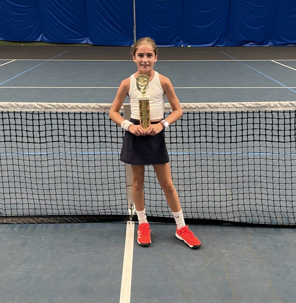 Little girl holding tennis trophy on court